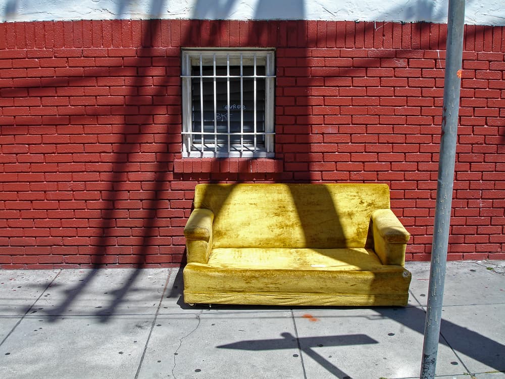 A vintage yellow velvet loveseat abandoned on a San Francisco street under a one-way sign